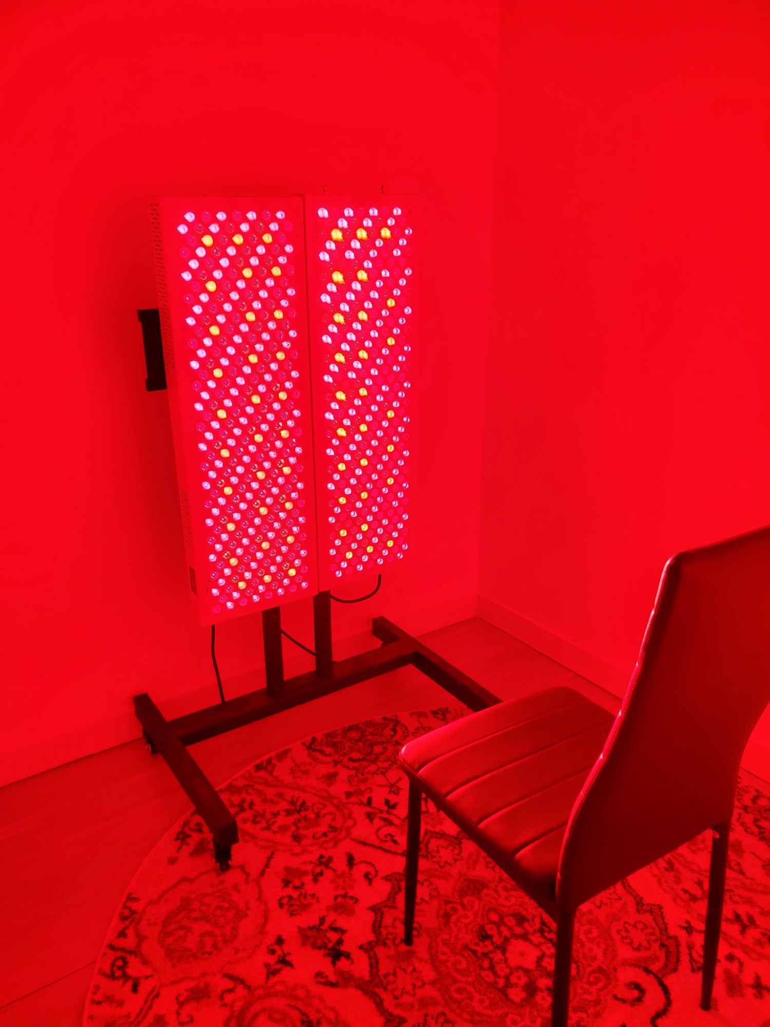 Red and near-infrared light therapy panels glowing beside a chair in a treatment room at fhL Massage & Wellness
